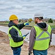 Two men in PPE in conversation beside construction area with stormwater.