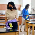Two adults clean desks in classroom.