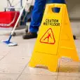 Janitor mops by a caution wet floor sign.