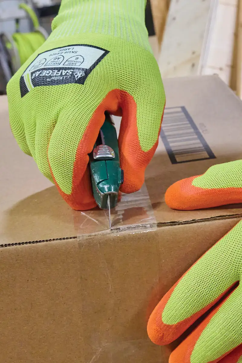 A worker opening a box with a box cutter while wearing proper PPE